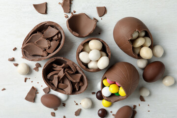 Broken chocolate eggs with candies on white wooden table, flat lay