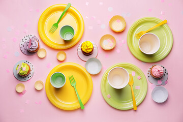 Plastic tableware and cupcakes on color background