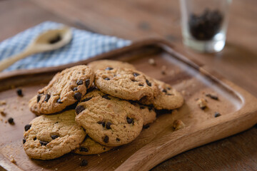Homemade stacked chocolate chip cookies on wooden plate for coffee break