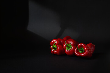 Three whole red sweet bell peppers isolated on black background with light and copy space
