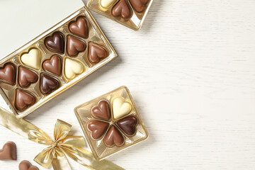 Beautiful heart shaped chocolate candies in boxes on white wooden table, flat lay with space for text