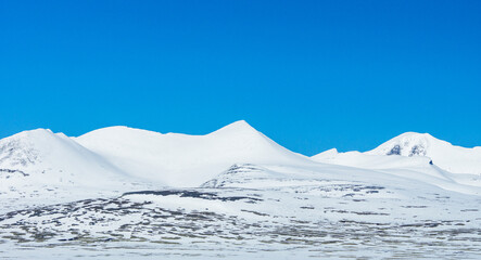 Snow capped mountain peaks against blue sky.