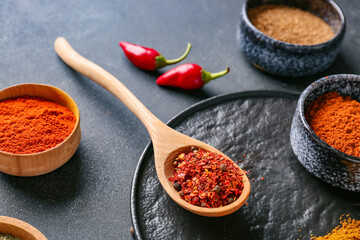 Bowls and spoon with different spices on dark background, closeup