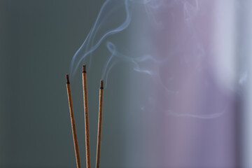 Incense sticks smoldering on blurred background, closeup. Space for text