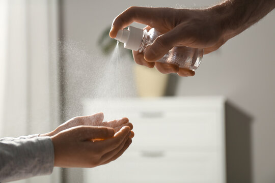 Man spraying antiseptic onto child's hands indoors, closeup - Powered by Adobe