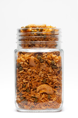 Hot spicy Kashmiri Mixture (Namkeen) snacks in a glass jar, made with dry fruits, peanuts, corn flakes, etc. Pile of Indian spicy snacks, under backlight, Front view