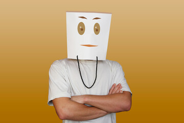 Young man hiding face behind paper bag with drawn emoticon on light background