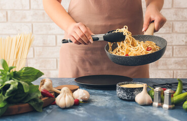 Woman putting noodles with chicken on plate in kitchen