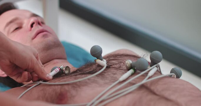 Hospital nurse fixing electrodes on patient limbs for cardiology test, equipment. doctor preparing male patient for removal of cardiogram. doctor fastens electrodes to patient. Install ECG suckers