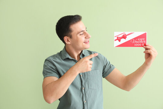 Handsome Young Man With Gift Voucher On Color Background