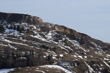 Fototapeta na wymiar hillside covered in patches of snow, during a warm winter
