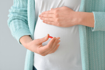 Pregnant young woman with pill on grey background, closeup