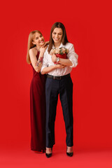Young transgender couple with flowers on color background. Valentine's Day celebration