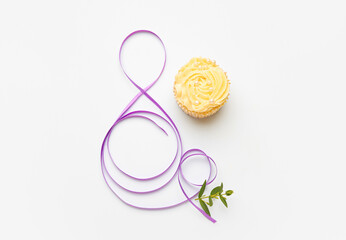 Figure 8 made of violet ribbon and cupcake on light background. International Women's Day celebration