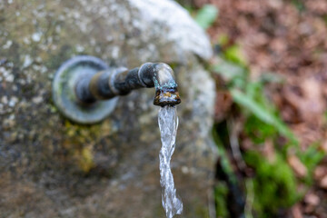 Wasser flieset aus einem gerosteten, alten Wasserhahn der am Felsen befestigt ist. 