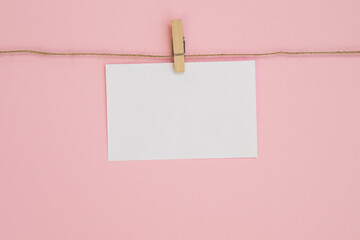 Empty paper sheet for notes, frames that hang on a rope with clothespin and isolated on pink background.