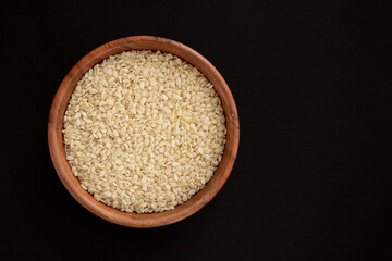 White sesame seeds in a bowl, isolated on black background.