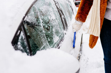 Bad weather conditions in winter. Transport, winter, weather, people and vehicle concept. unrecognizable woman cleaning snow with car brush.