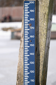 Gauge attached to a bollard in a frozen lake in the Netherlands, which indicates the water level in ditches and canals in relation to the normal Amsterdam level. Focus on the blue ruler 