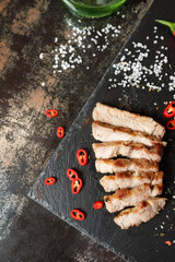 pork cooked in a pan and cut into pieces with spices on a dark stone background