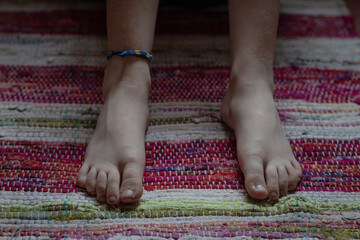 Pies de un niño, con pulcera sobre una alfombra
