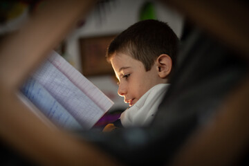 Fototapeta premium Niño de pelo corto escribe en su cuaderno con iluminación natural toma entre sillones 