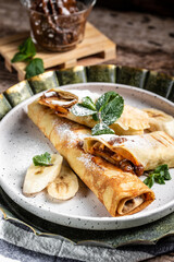 Crepes with chocolate cream and banana on white plate. Thin pancakes, blini. Delicious breakfast or snack. Food recipe background. Close up