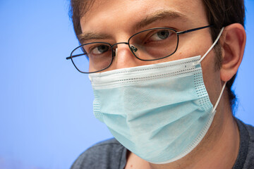 Caucasian male head with glasses and medical face mask studio portrait isolated on blue background
