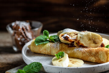 Crepes stuffed with chocolate spread and banana on white plate. Thin pancakes, blini. Delicious breakfast or snack. Food recipe background. Close up