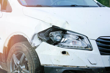 A car accident. A crashed white car with a damaged mudguard, hood, headlight and bumper.