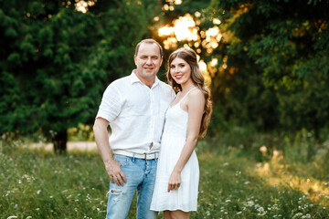 Young loving couple hugging on the green grass in the park. Beautiful woman and man gently touch each other. Beautiful couple in love. girl in the dress and the guy in the shirt. valentines day