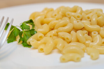 Boiled yellow pasta on a white plate with a fork