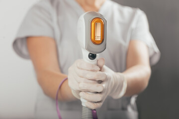 A woman tunes a laser hair removal machine. She holds a working part of the epilator in her hands and poses for a photo. It is located in a modern beauty salon. Body Care. Underarm Laser Hair Removal.