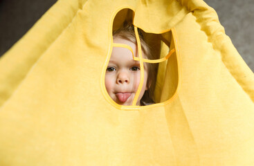 A little girl looks out the window of a teepee shows her tongue playing at home on the couch.