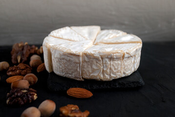 Head of brie cheese on plates of black slate and assorted nuts, almonds, hazelnuts and walnuts.Appetizer plate with cheese