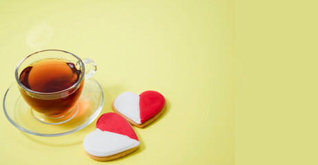 A red and white heart-shaped cookie next to a clear glass cup of tea
