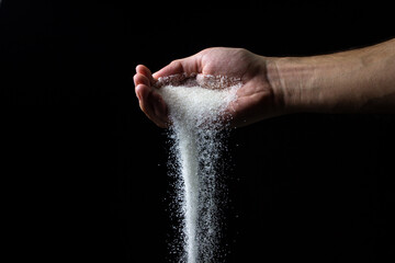 Sugar on a black background. Sugar pours from a man's hand. Excessive sugar intake
