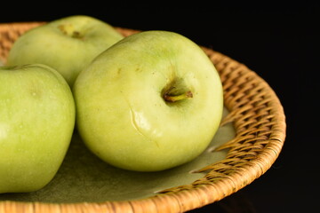 Several natural green apples by Renet Simirenko with a ceramic plate, close-up, isolated on black.