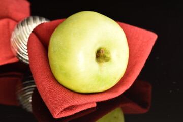 One natural green apple by Renet Simirenko with a red linen napkin, close-up, isolated on black.