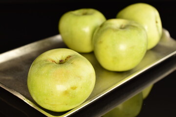 Several natural green apples by Renet Simirenko on a metal tray, close-up, isolated on black.