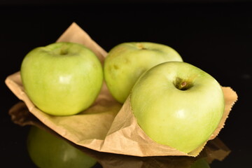 Three natural green apples by Renet Simirenko with a paper bag, close-up, isolated on black.