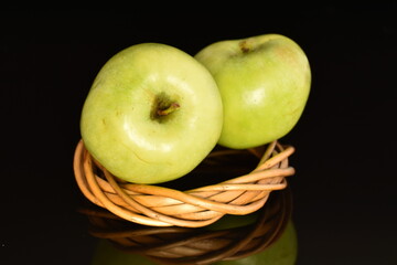 Two natural green apples by Renet Simirenko with a vine wreath, close-up, isolated on black.