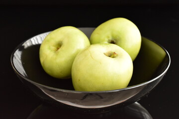 Three organic green apples by Renet Simirenko in a black plate, close-up, isolated on black.