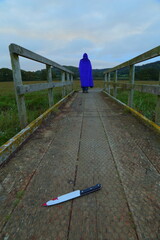 Man dressed in blue hood walk away from bloody knife on wooden footpath