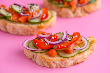 Brusketta on a pink background. Salmon, cucumber, bell peppers and sesame seeds on toasted bread.