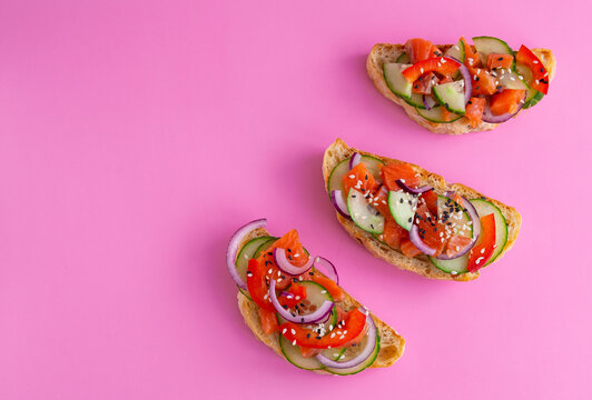 Brusketta on a pink background. Salmon, cucumber, bell peppers and sesame seeds on toasted bread. View from above