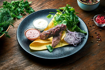 An appetizing dish of Turkish cuisine - beef kebab from minced meat with pita bread, cilantro, onions and sauces, served in a blue plate on a wooden background. Restaurant food. Close up view