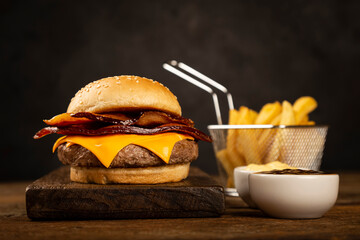 Tasty hamburger with french fries and sauces on dark background.