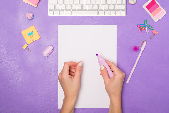 Bright vivid Flat lay workspace. Woman's hand ready for writing on blank list. Items on bright violet purple background, top view. Girly work desktop. School concept. 