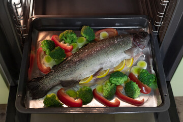 whole uncooked rainbow trout with broccoli, leek, paprika, and spices on baking tray in oven. Seafood concept. selective focus